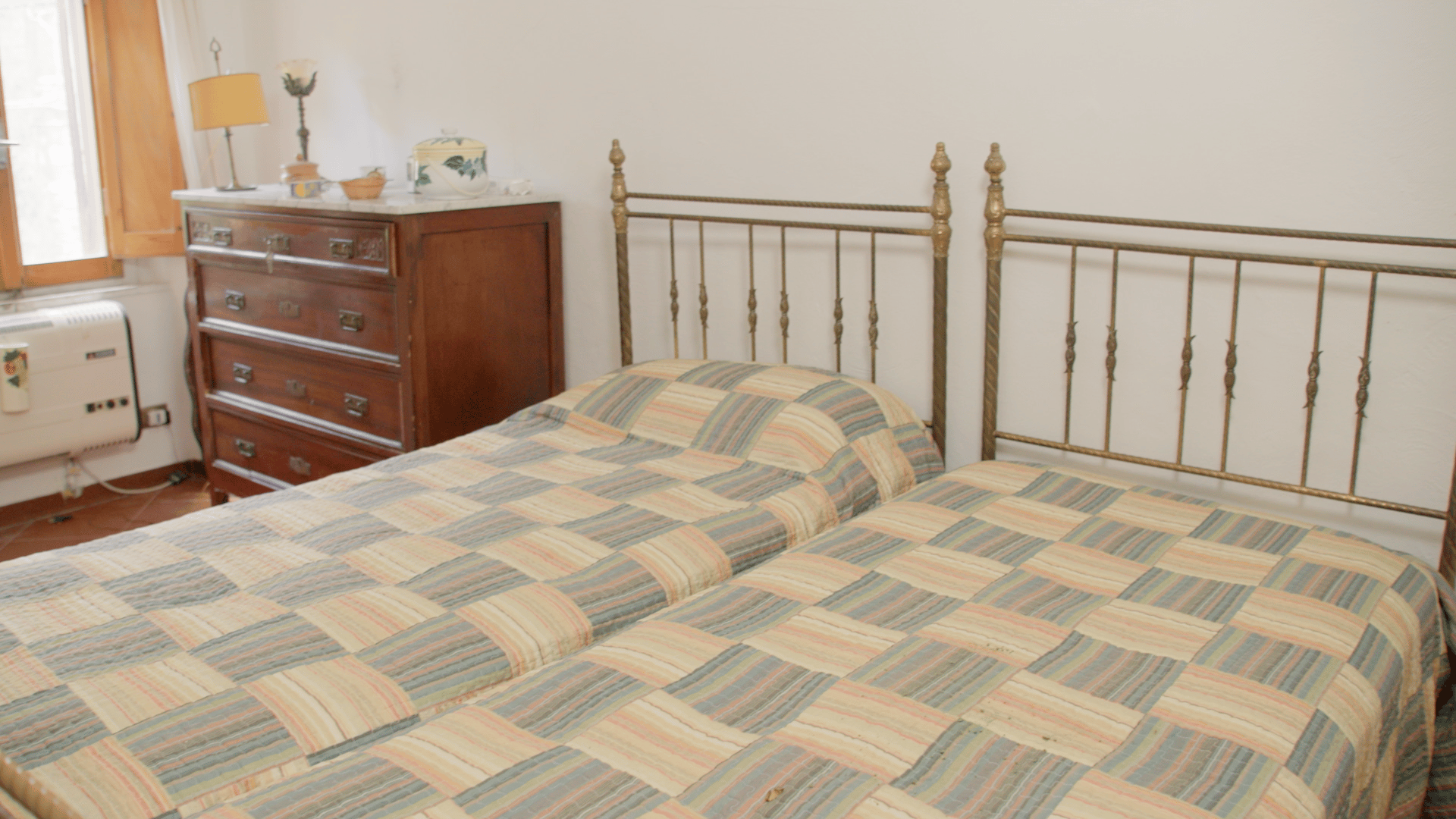 Two twin beds with patterned bedspreads, metal headboards, a wooden dresser, and a window.
