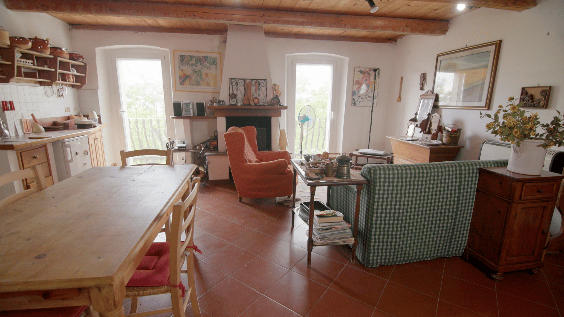 A rustic open-plan living room and kitchen with a wooden dining table, orange armchair, and green sofa.