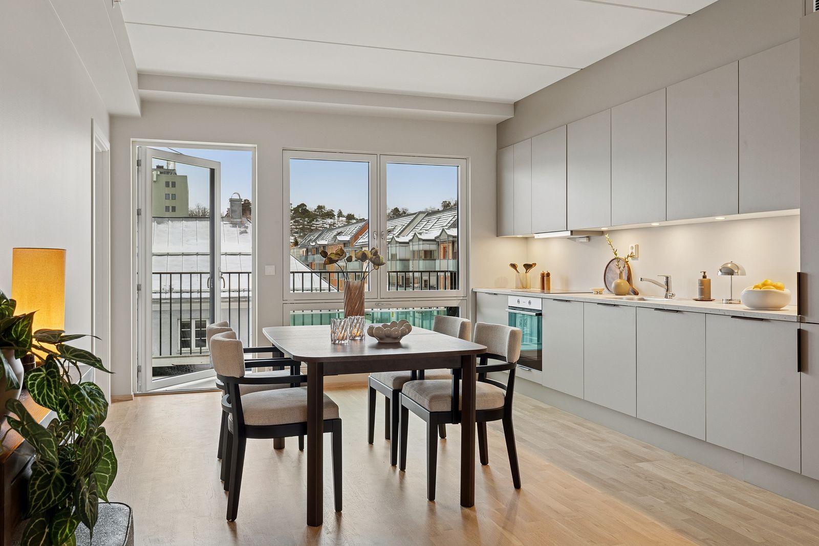 Modern open-plan kitchen and dining area with a light wood floor, balcony, and snowy city view.