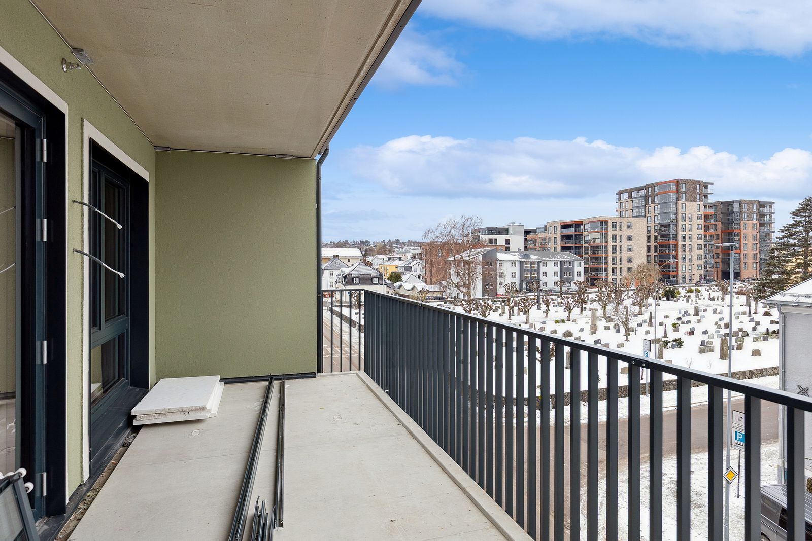 Balcony view of a snowy cemetery and city buildings under a cloudy blue sky.