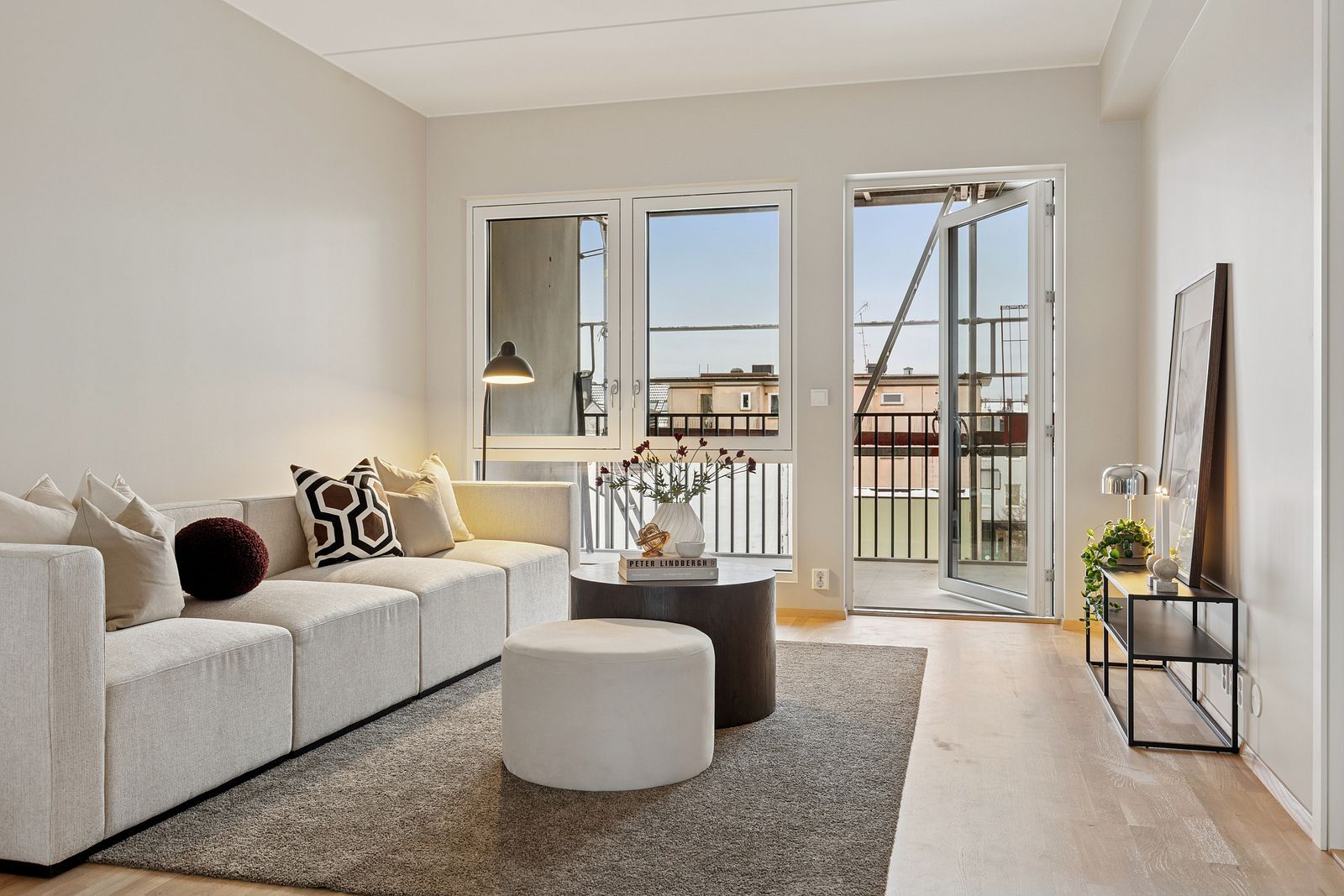 A bright, modern living room with a cream modular sofa, coffee table, and a balcony view through large windows.