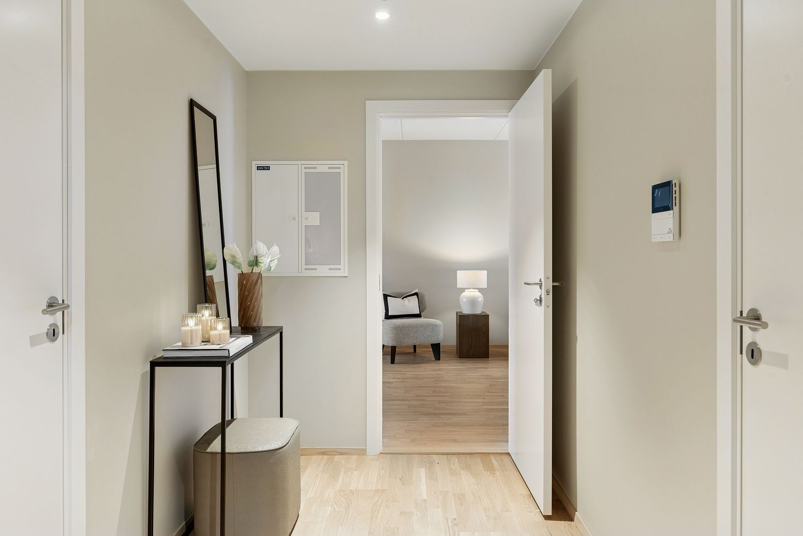 A modern, neutral-toned hallway with a console table, mirror, and an open door to another room.