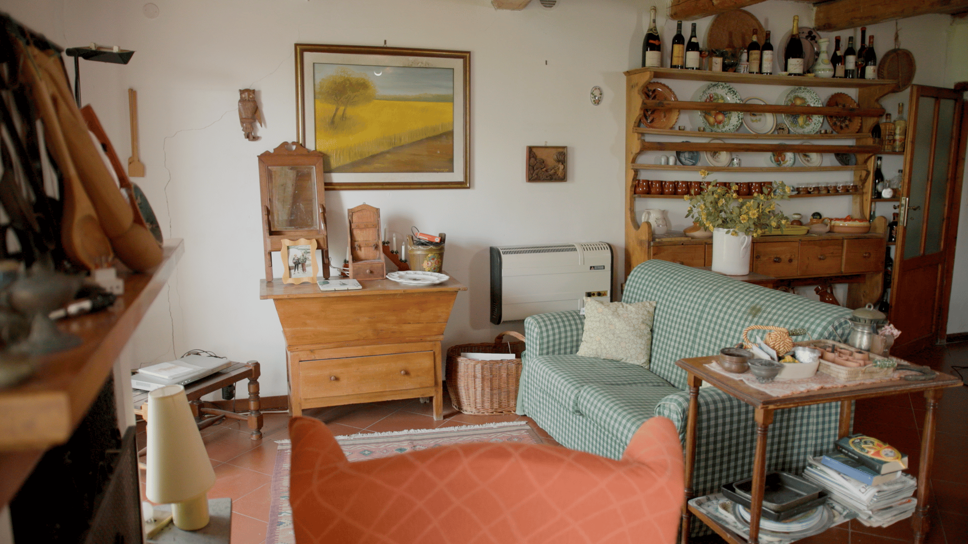 A rustic living room with a painting, wooden furniture, a green plaid sofa, and a large dish shelf.