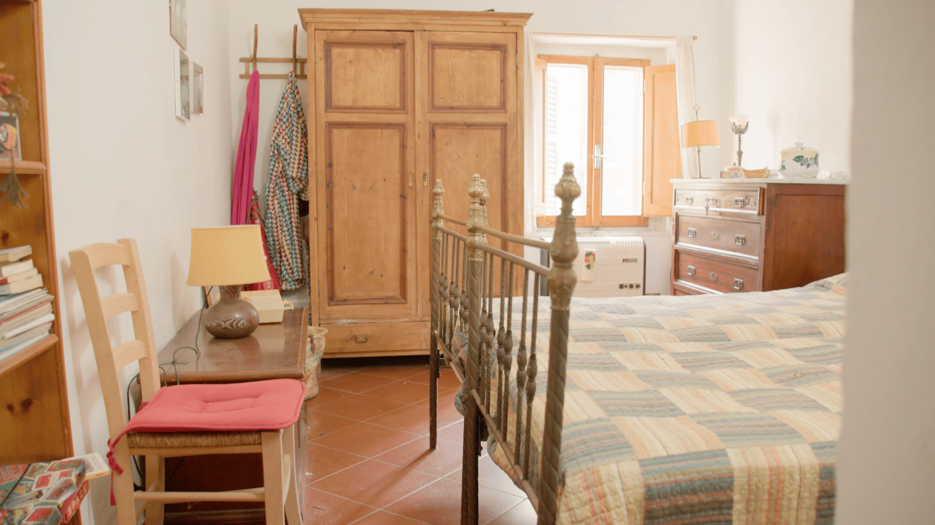 A rustic bedroom featuring a metal bed, wooden wardrobe, dresser, and a window with natural light.