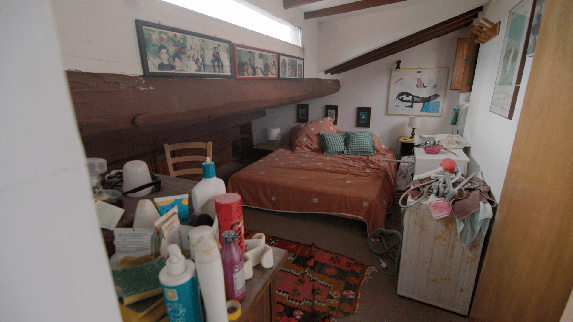 A cluttered bedroom featuring a bed with orange bedding, a laundry machine, and various household items.