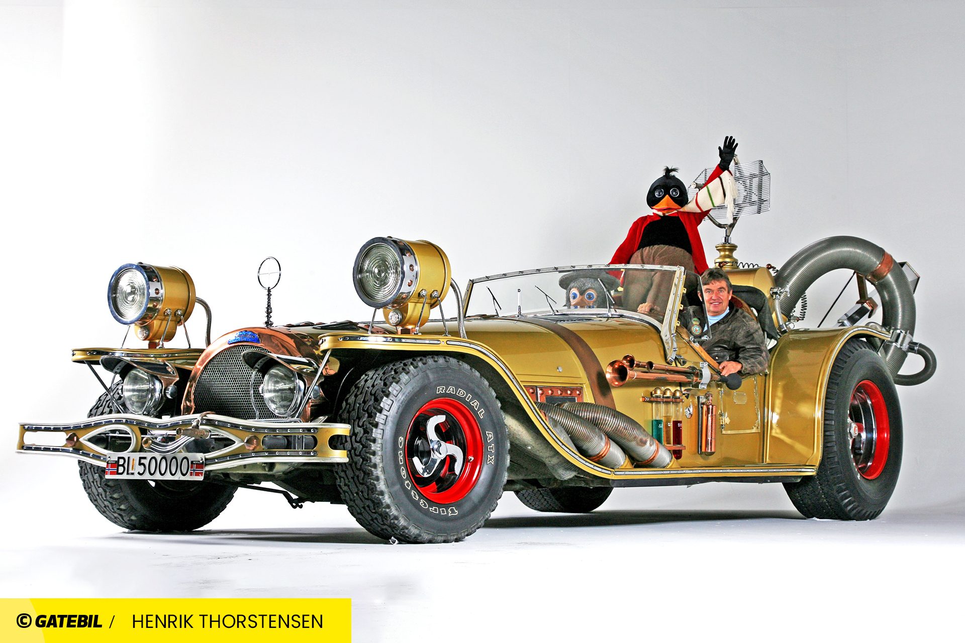 A man and two large puppets ride in a bizarre, fantastical gold car.