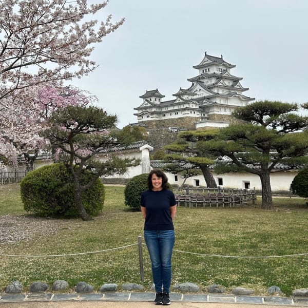 Woman smiles in front of Himeji Castle and cherry blossoms.