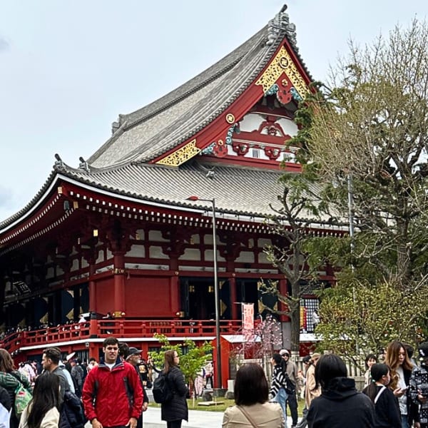 Red Japanese temple with a multi-tiered roof, crowded with people and trees in the foreground.