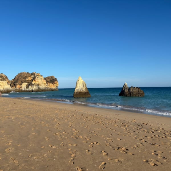 A golden sandy beach stretches towards turquoise waters, dotted with distinctive sea stacks under a clear blue sky.