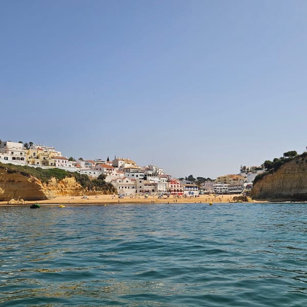 Coastal town with white buildings on sandy cliffs and a golden beach, seen from the sea.