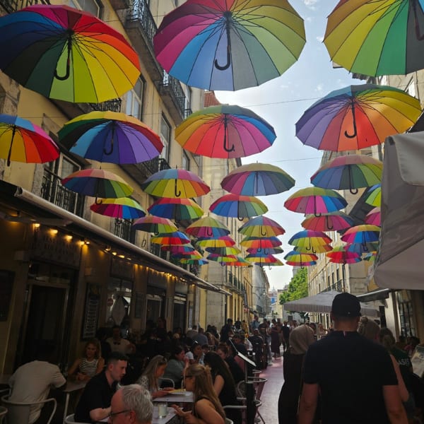 A vibrant street scene with countless colorful rainbow umbrellas strung above a busy outdoor dining area.