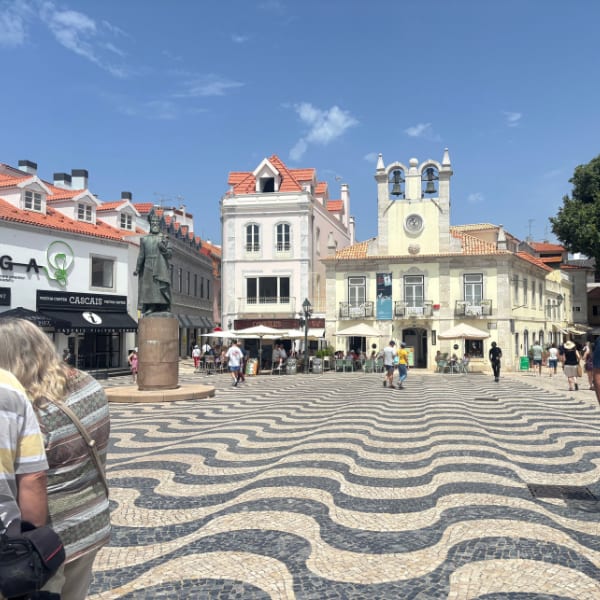 Bustling Cascais town square with a statue, historic buildings, and distinctive wavy mosaic pavement.