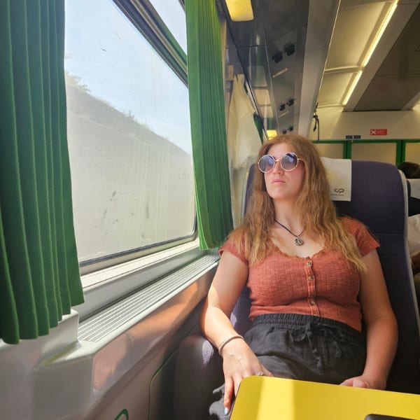 Woman with sunglasses looking out the window while sitting in a train on a sunny day.