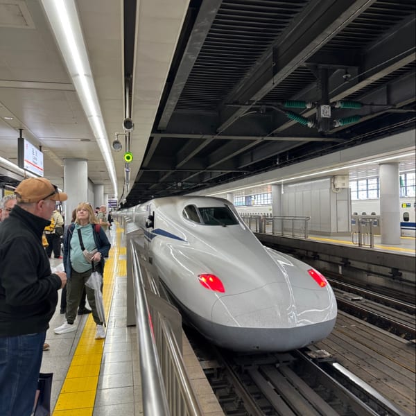 Japanese Shinkansen bullet train at a station platform with people.