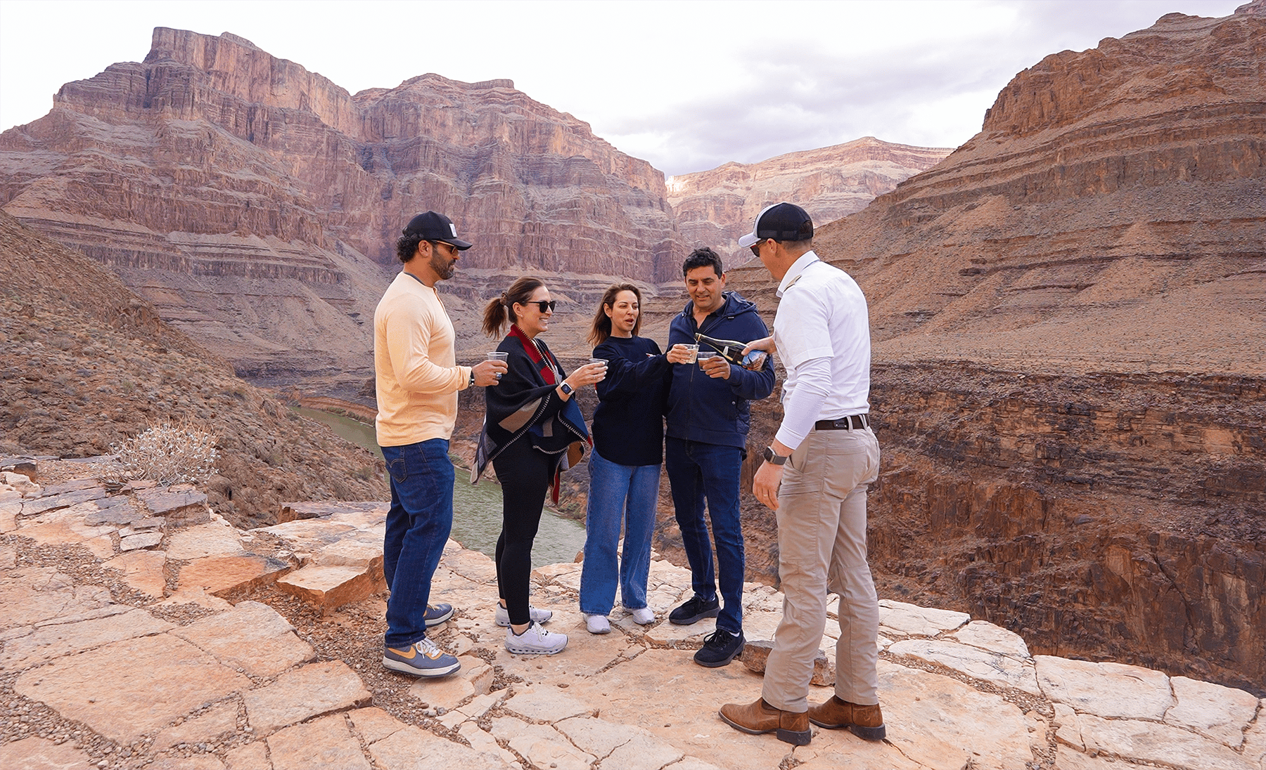 Five people toasting at a vast canyon overlook with a river below.