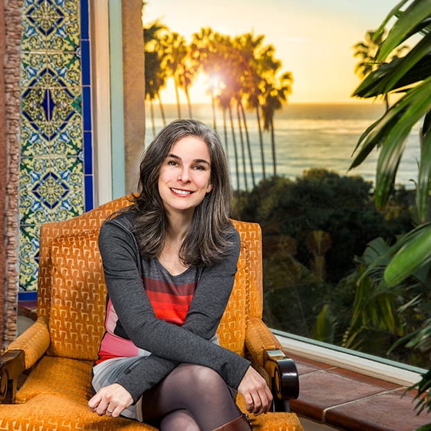Smiling woman in armchair, ocean sunset view with palm trees.