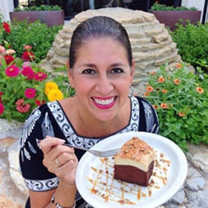 Smiling woman holding cake slice and fork outdoors.