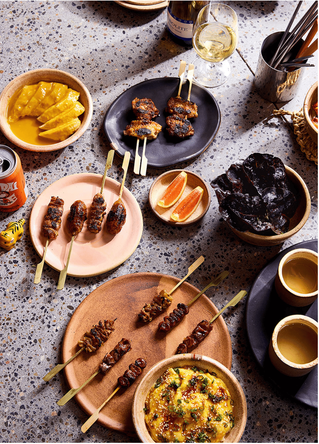 Skewers, bowls of food, and drinks on a table.