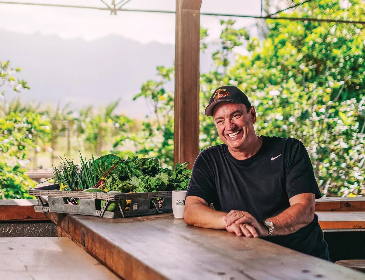 Laughing man in a cap by fresh greens on a wooden table, outdoors.