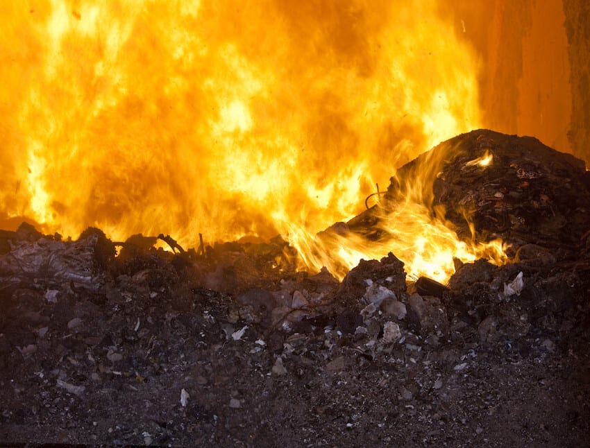 Intense orange flames engulf a large pile of burning waste.