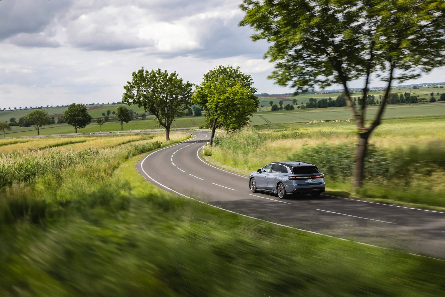 Grey wagon on winding road through green fields, motion blur.