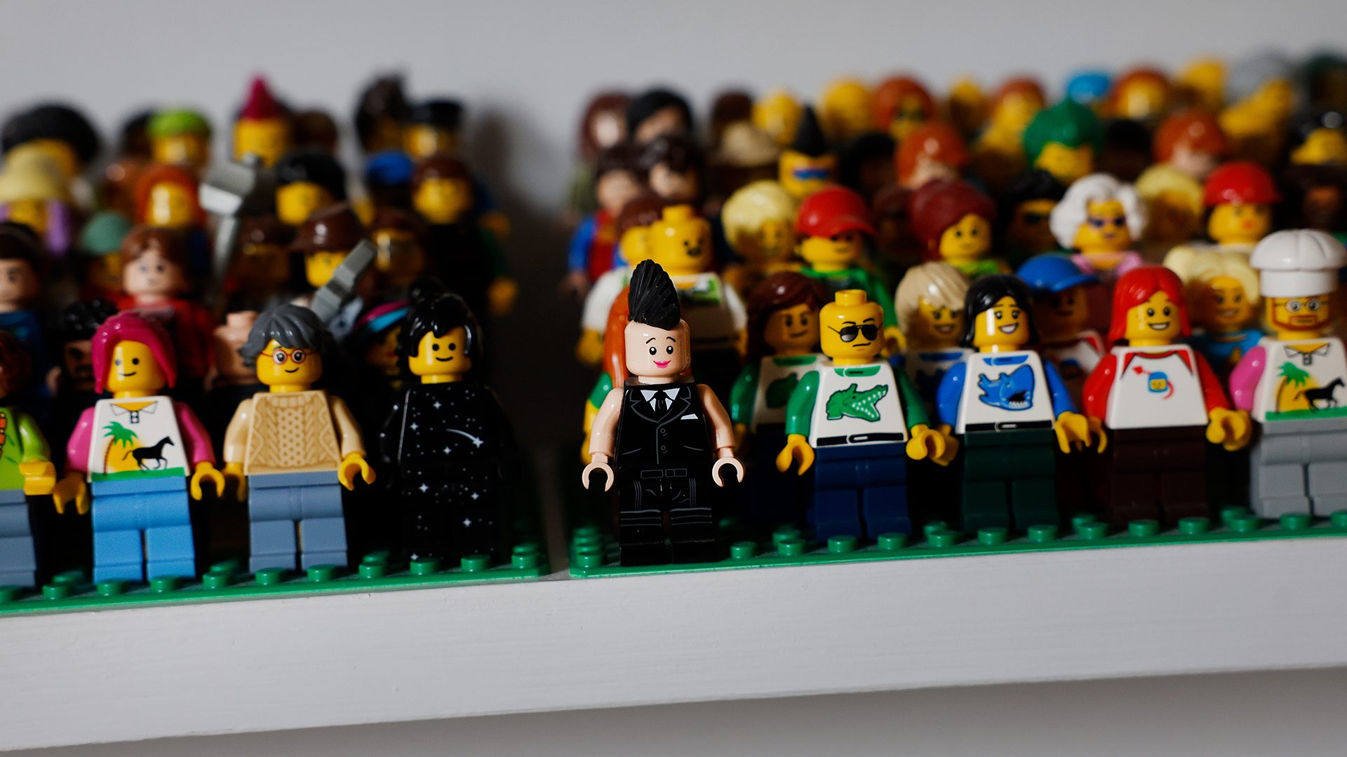 A diverse group of Lego minifigures stands on a shelf, some in focus, many blurred.