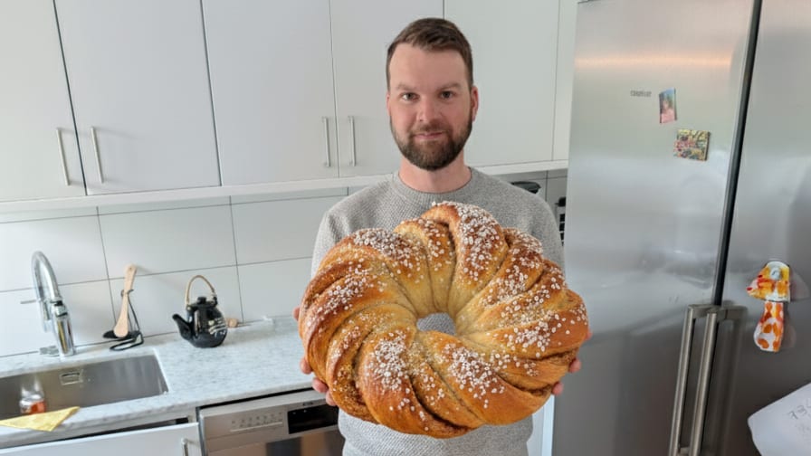 Man in kitchen holding a large, sugar-topped braided bread.