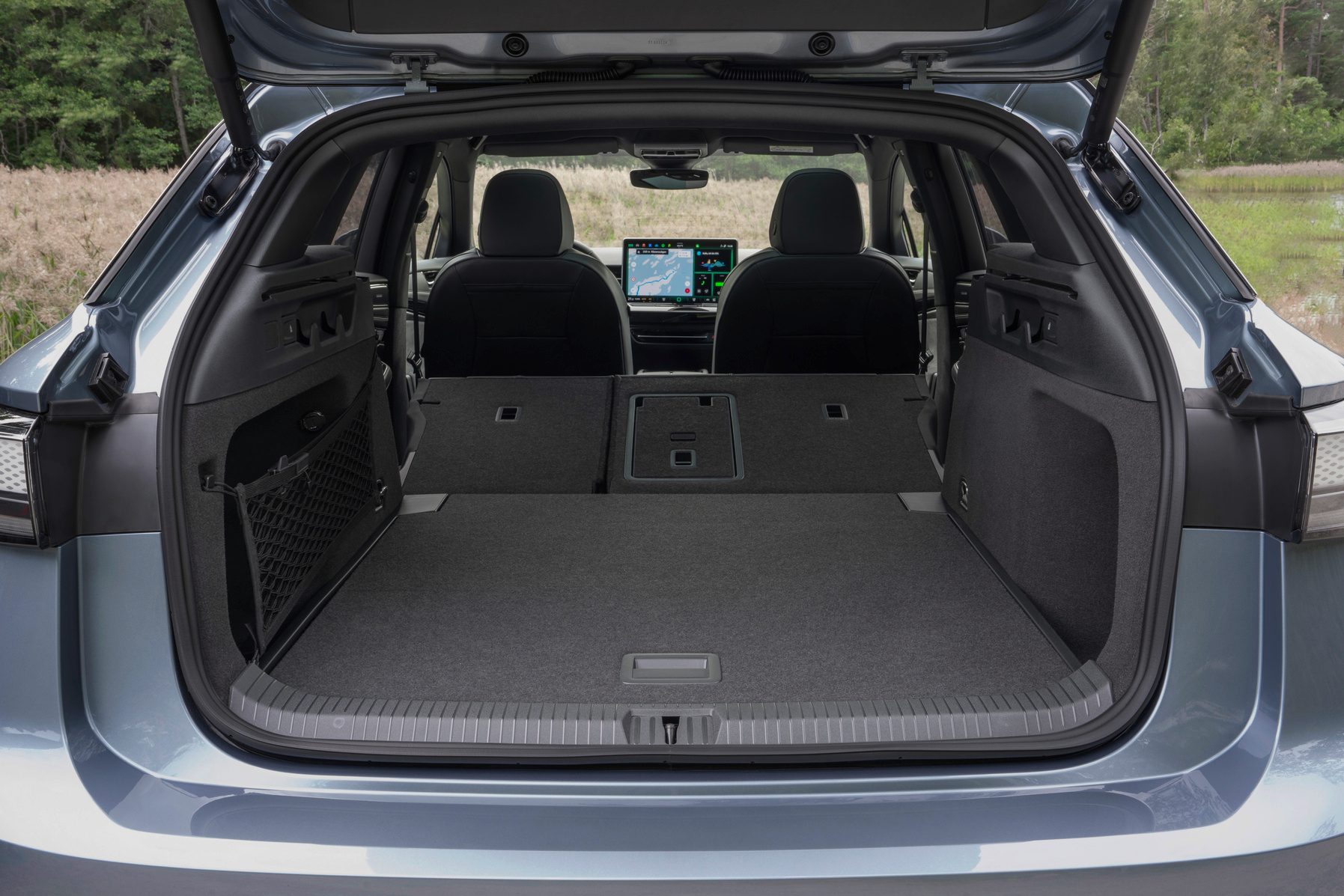 Open trunk of a blue car revealing spacious cargo area and the cabin with digital screens.
