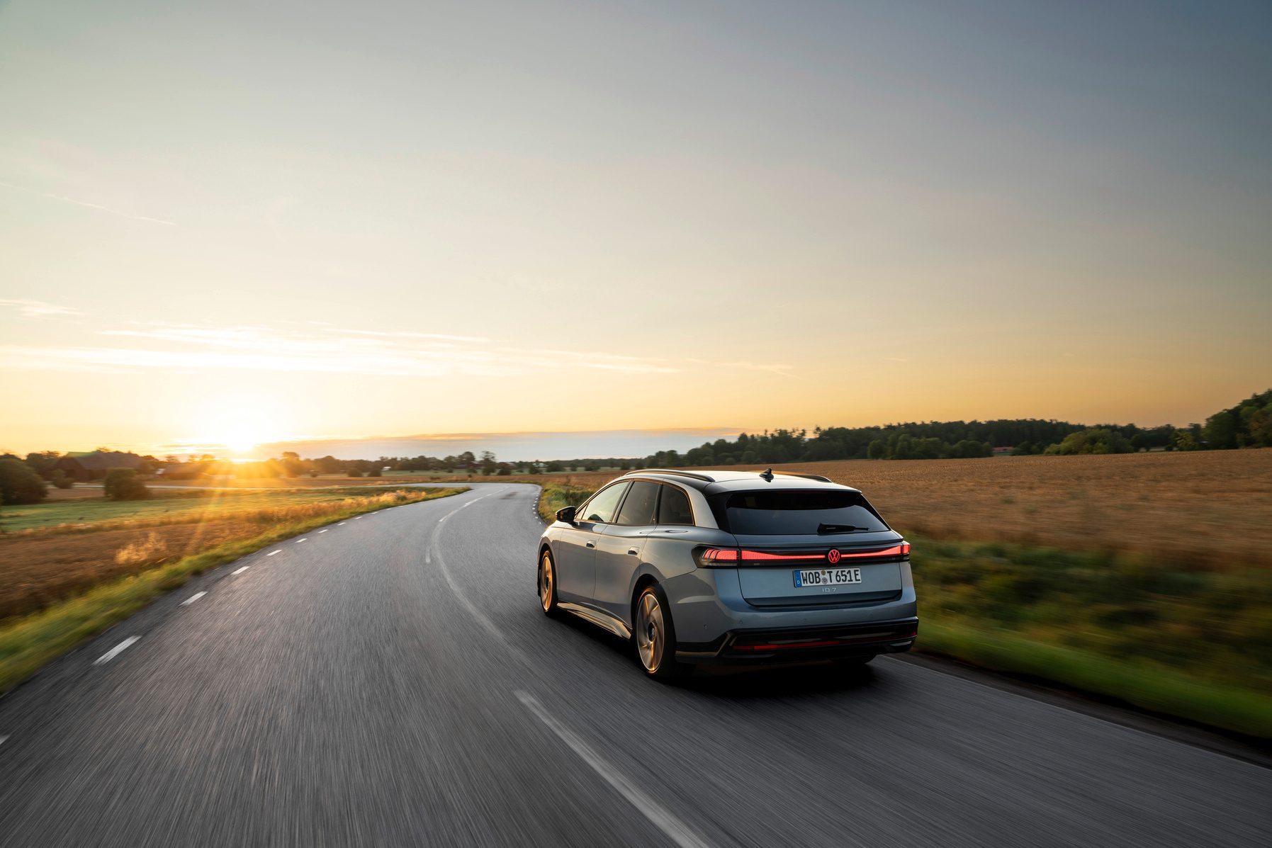 Grey station wagon driving on a curved road at sunset.