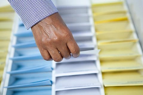 A hand extracts a white card from a filing tray with organized blue, white, and yellow compartments.