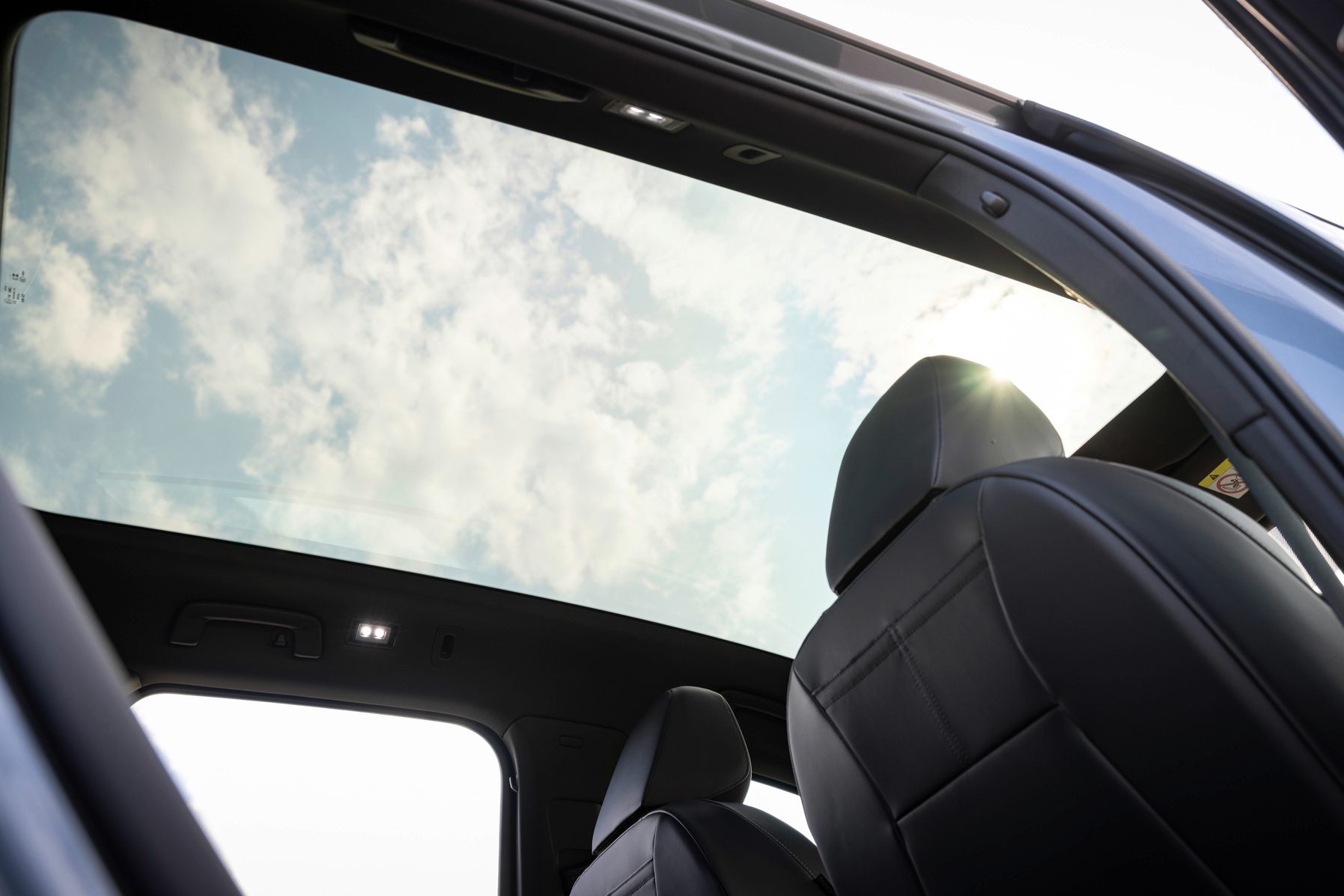 Car interior with panoramic sunroof showing cloudy sky and black seats.