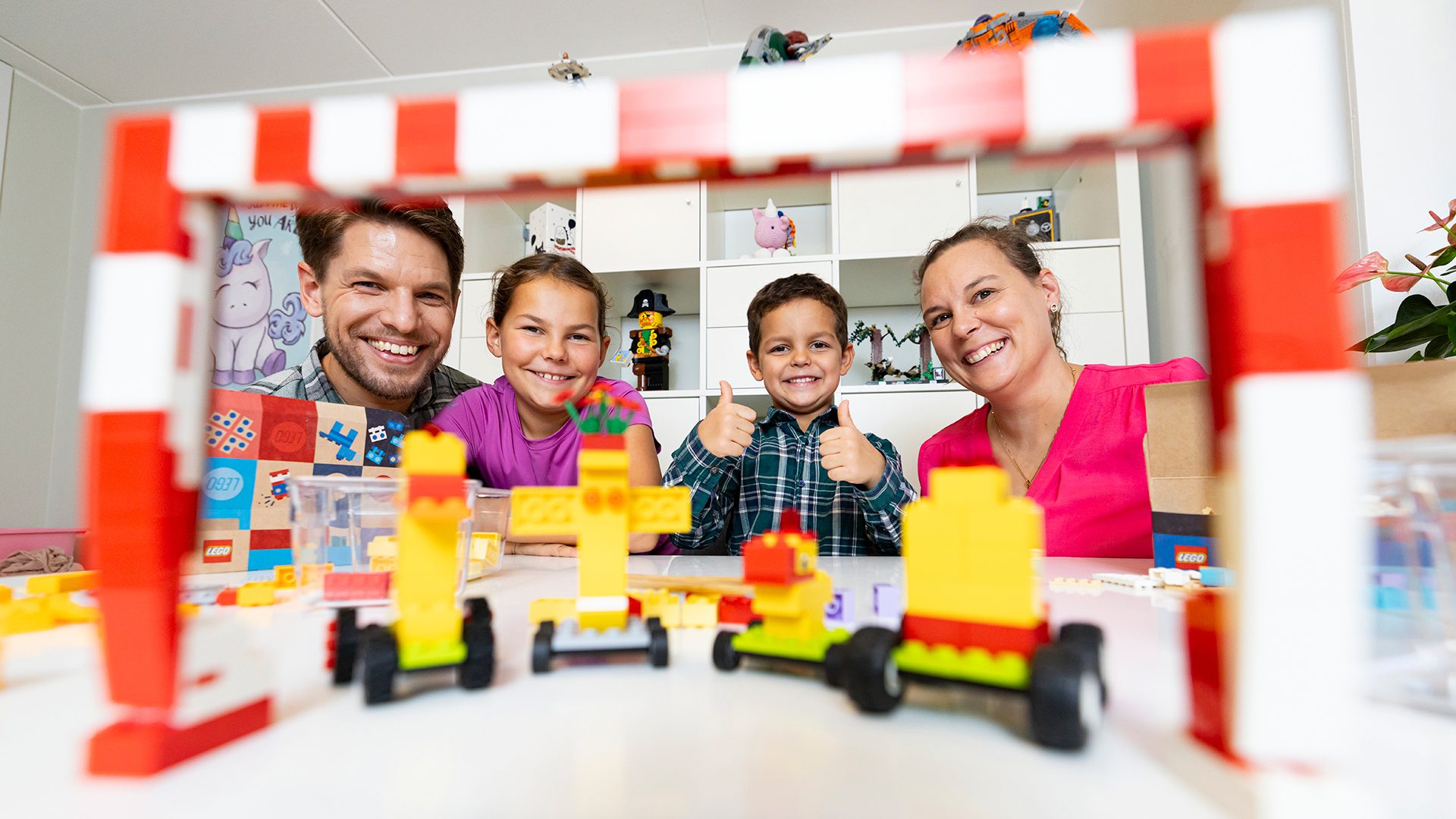 Happy family with kids giving thumbs up behind Lego builds.