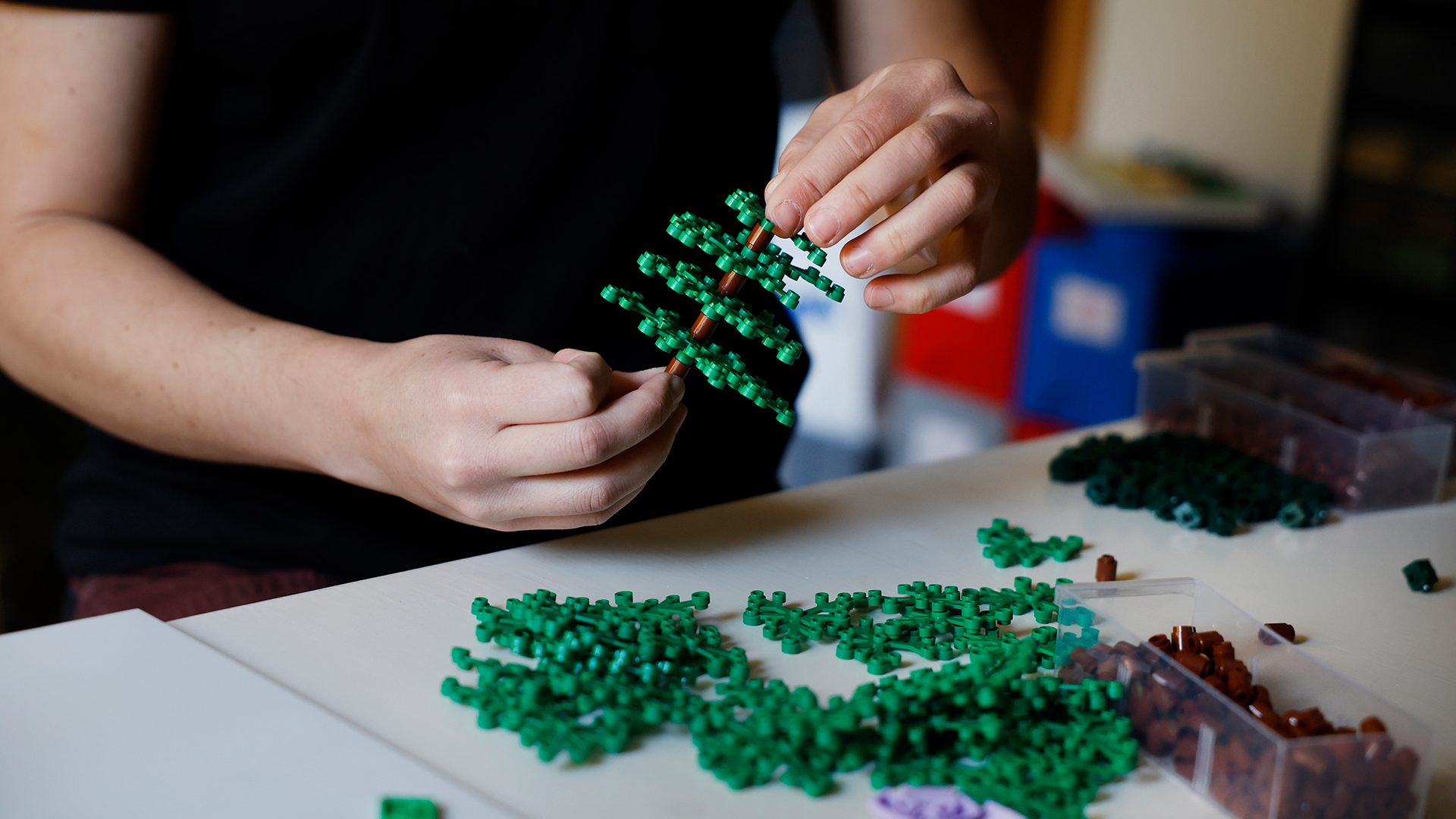 Close-up of hands assembling a LEGO tree from green and brown bricks.