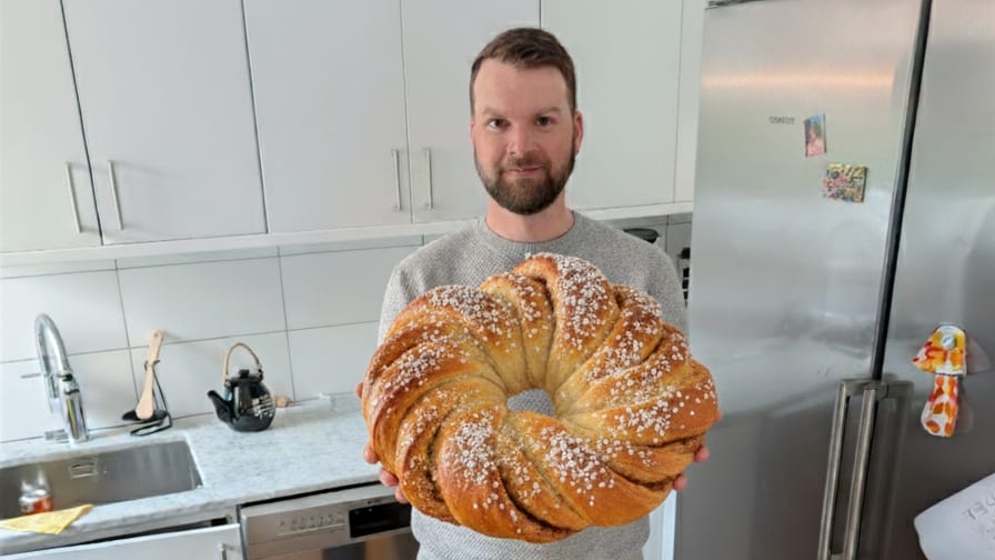 Man in a kitchen holding a large, round, braided sweet bread.
