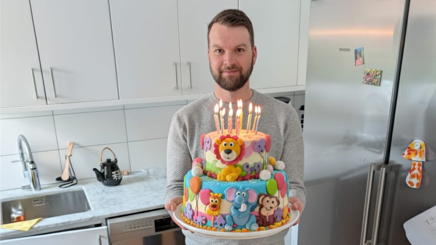 Man holding a birthday cake with animal figures and lit candles.