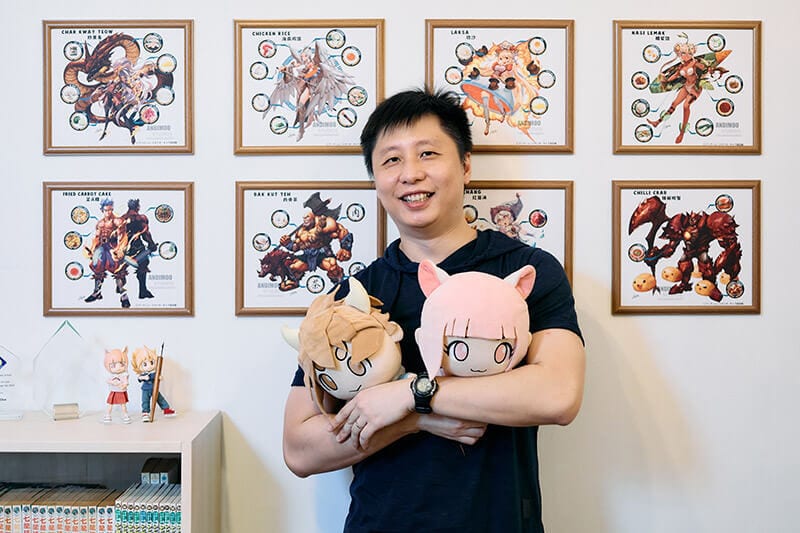 Smiling man holding plushies, surrounded by framed anime-style art prints of Asian dishes.
