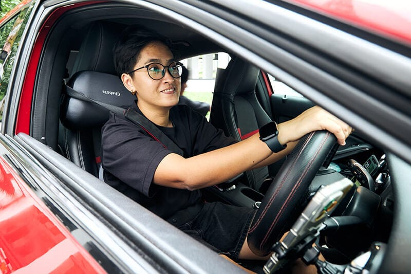 Person with glasses at the wheel of a red car.