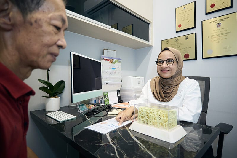 A doctor in a hijab points to a document for an older male patient in a clinic.