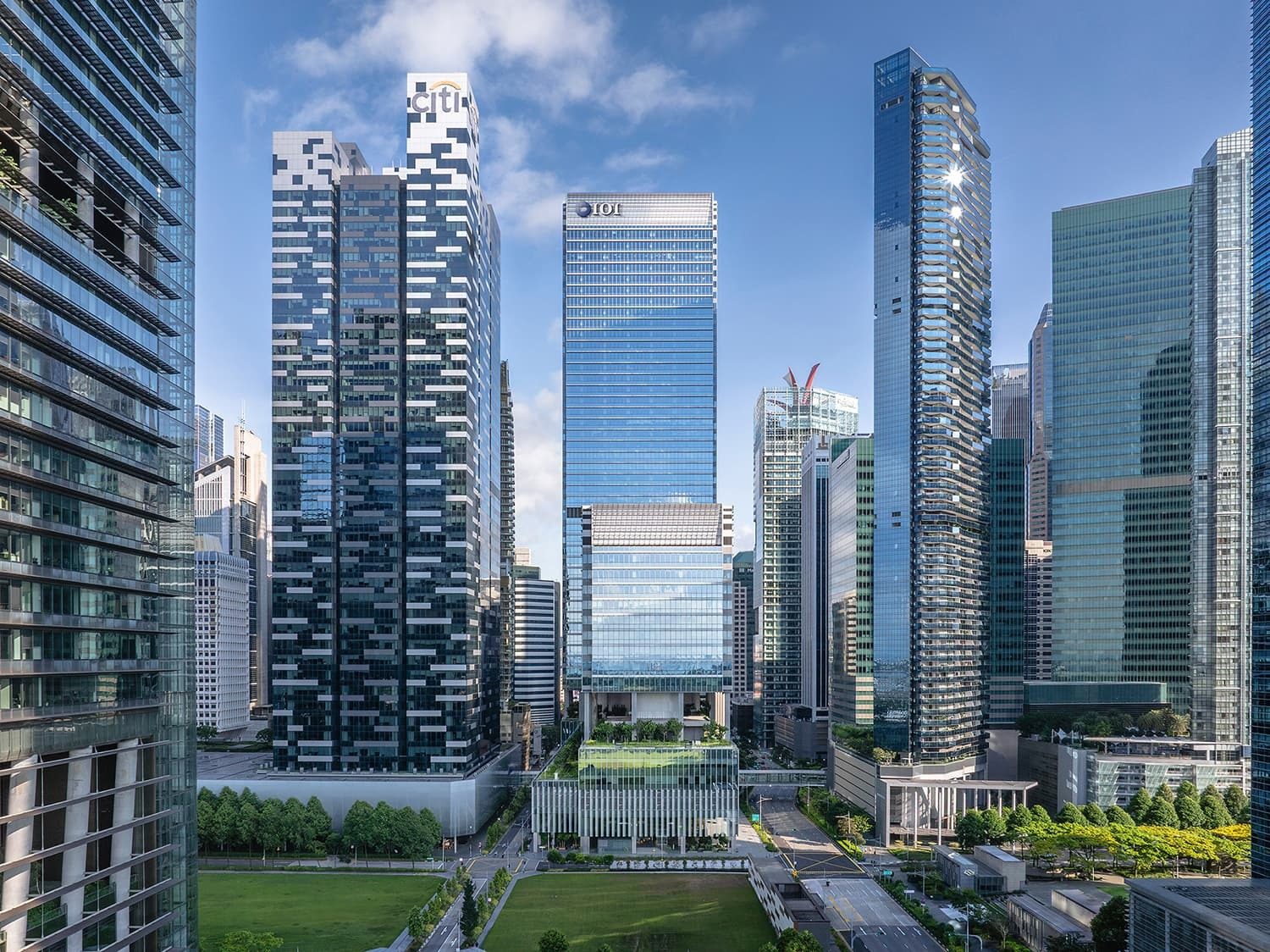 Tall modern skyscrapers in a city with green parks and a bright blue sky.