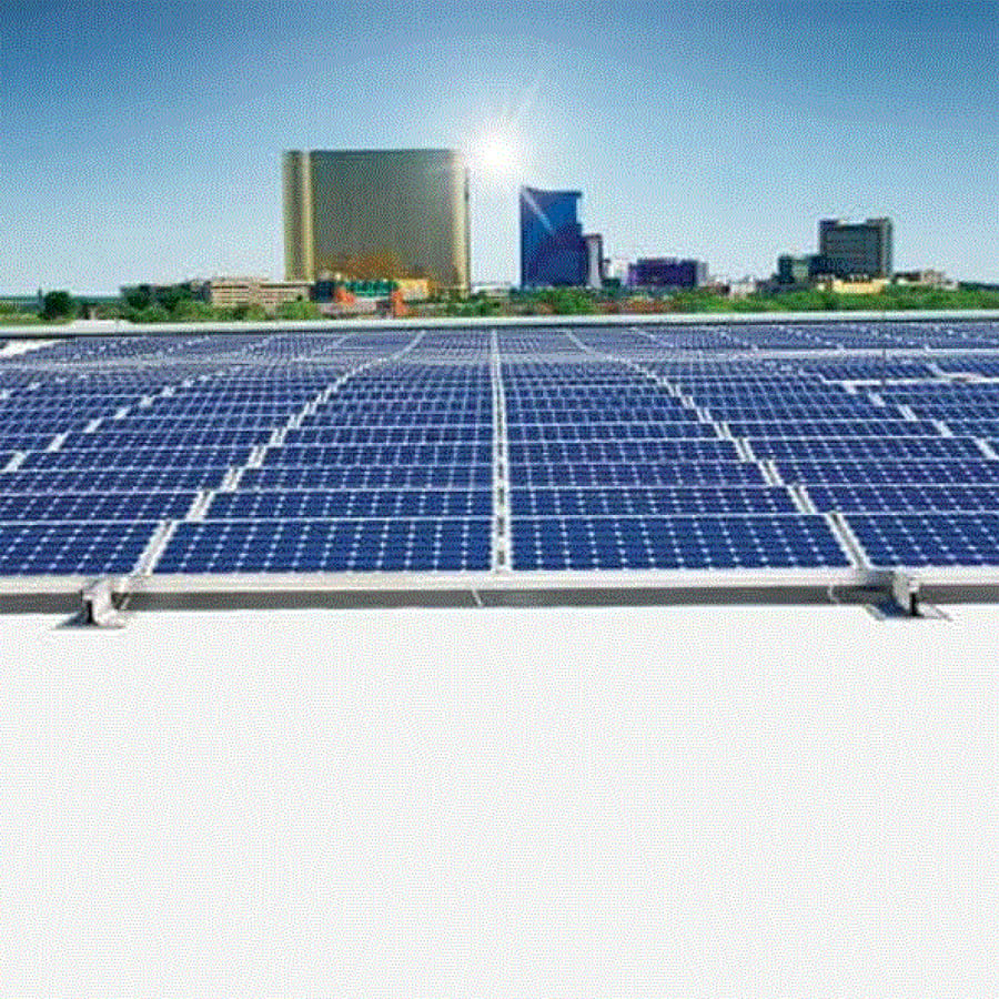 Closeup of blue solar panels on a commercial roof with a city skyline in the distance all under a sunny blue sky.