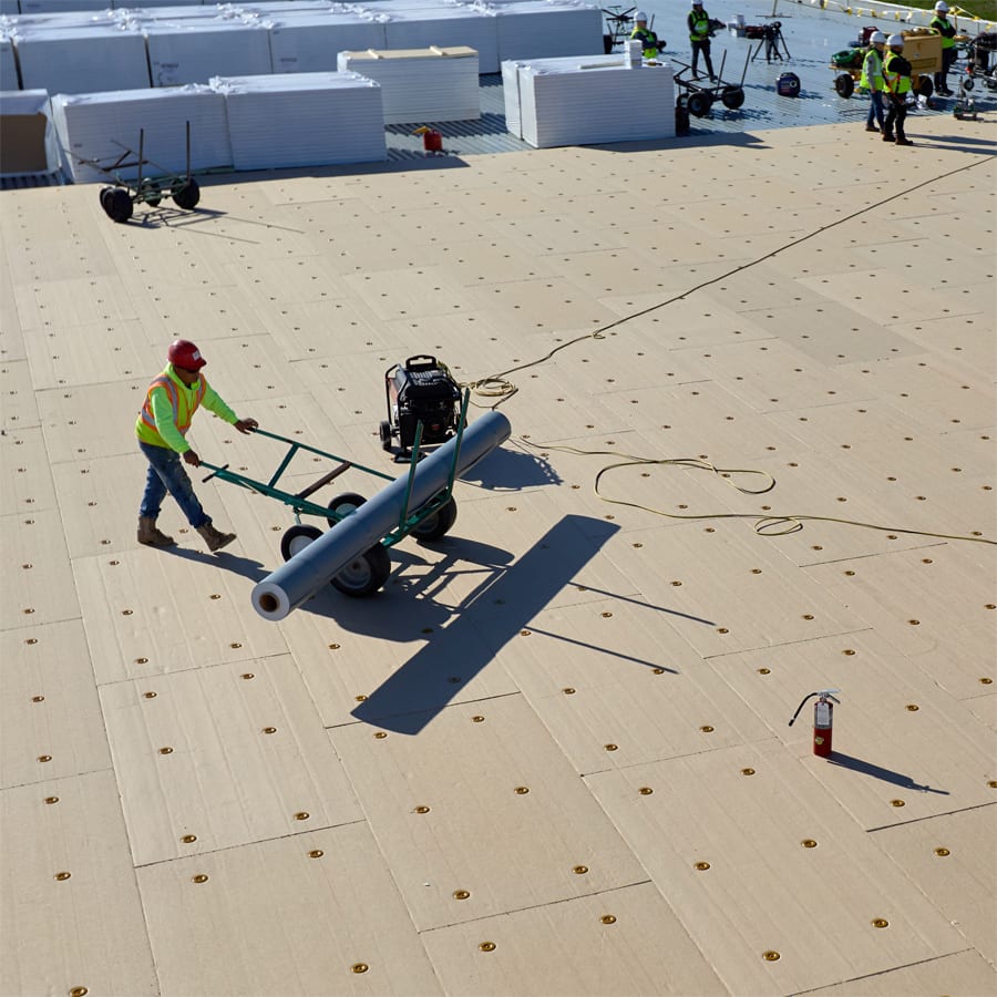 Roofer using a cart to move a roll of roofing insulation.