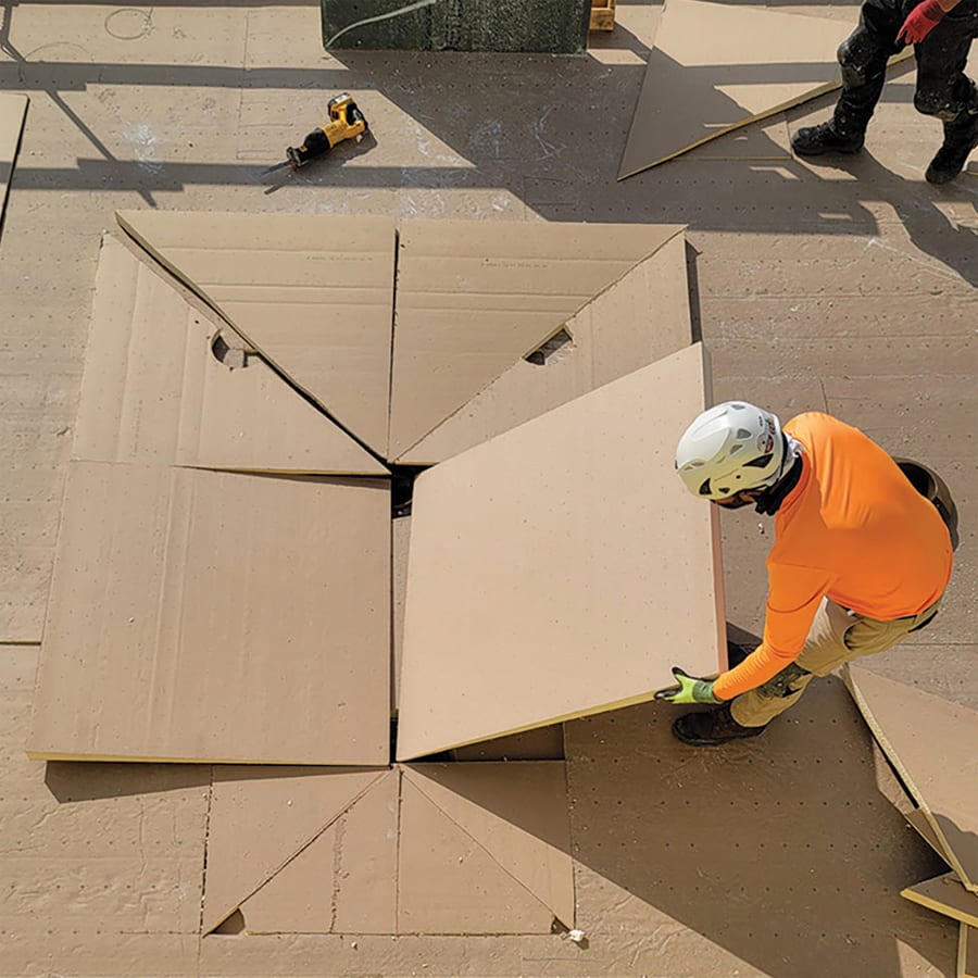 Worker installing a large building panel into a floor opening surrounded by other panels.