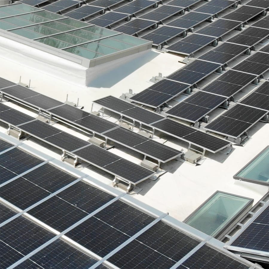 Black solar panels between skylights on a commercial roof.