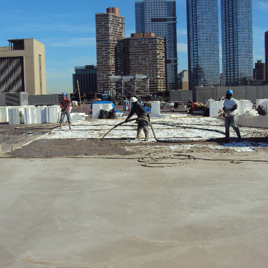 Roofers applying lightweight insulating concrete with hoses under a blue sky.