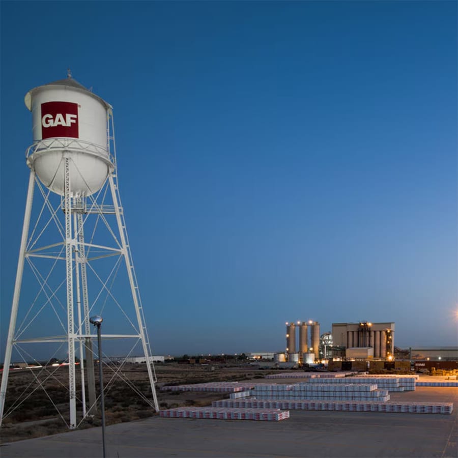 Water tower with GAF logo at night with refinery in distance