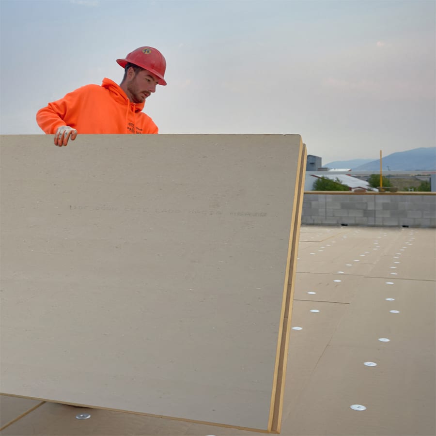 Worker in hard hat holds large panel on a rooftop.