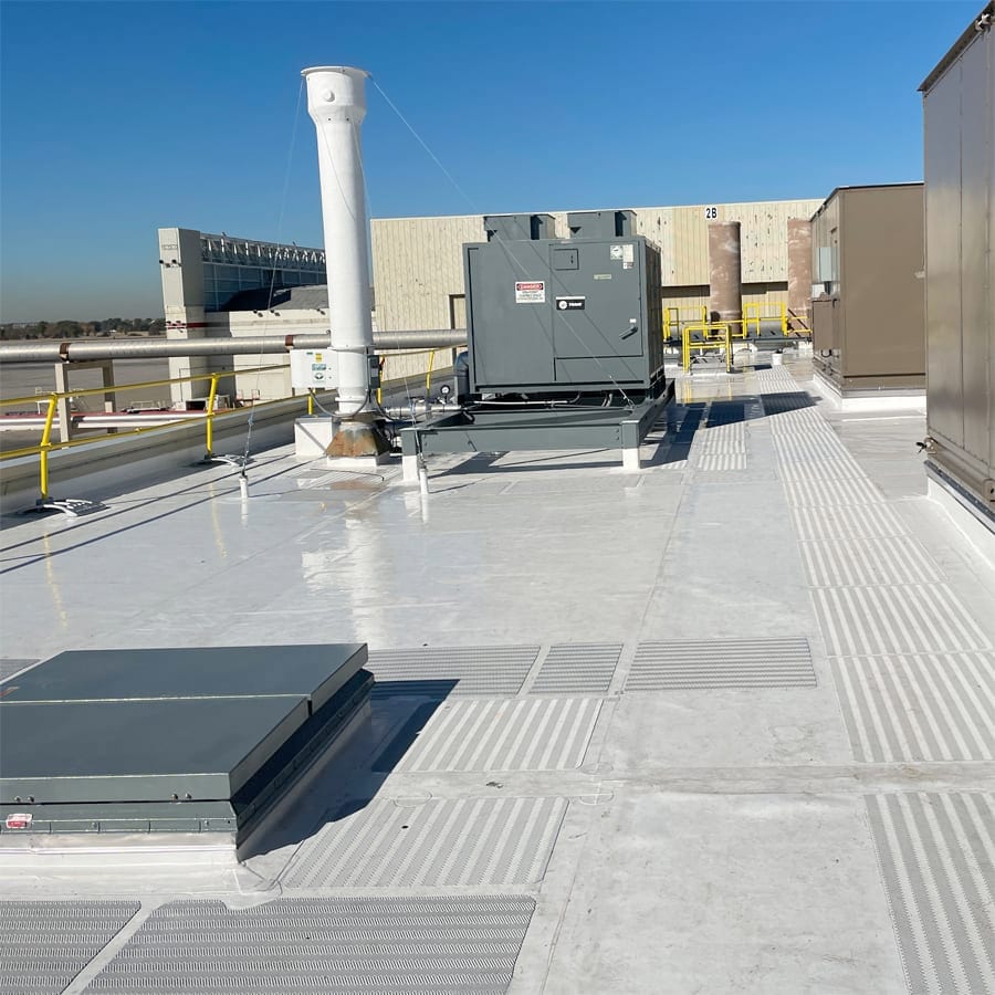 Industrial rooftop with HVAC equipment, tall vent pipe, and gridded walkways under a clear sky.