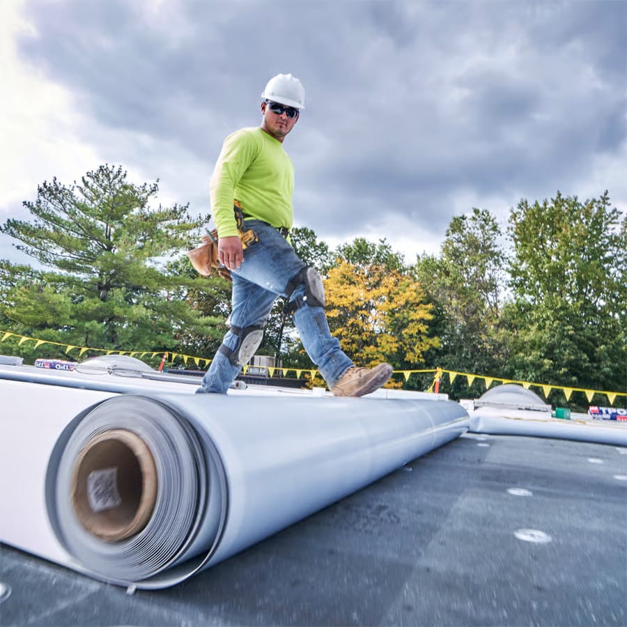 Roofer in hard hat unrolling membrane on a roof.