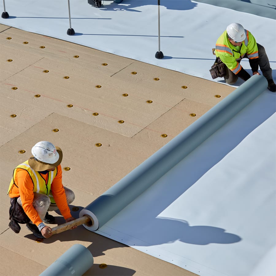 two roofers unrolling single-ply roof material