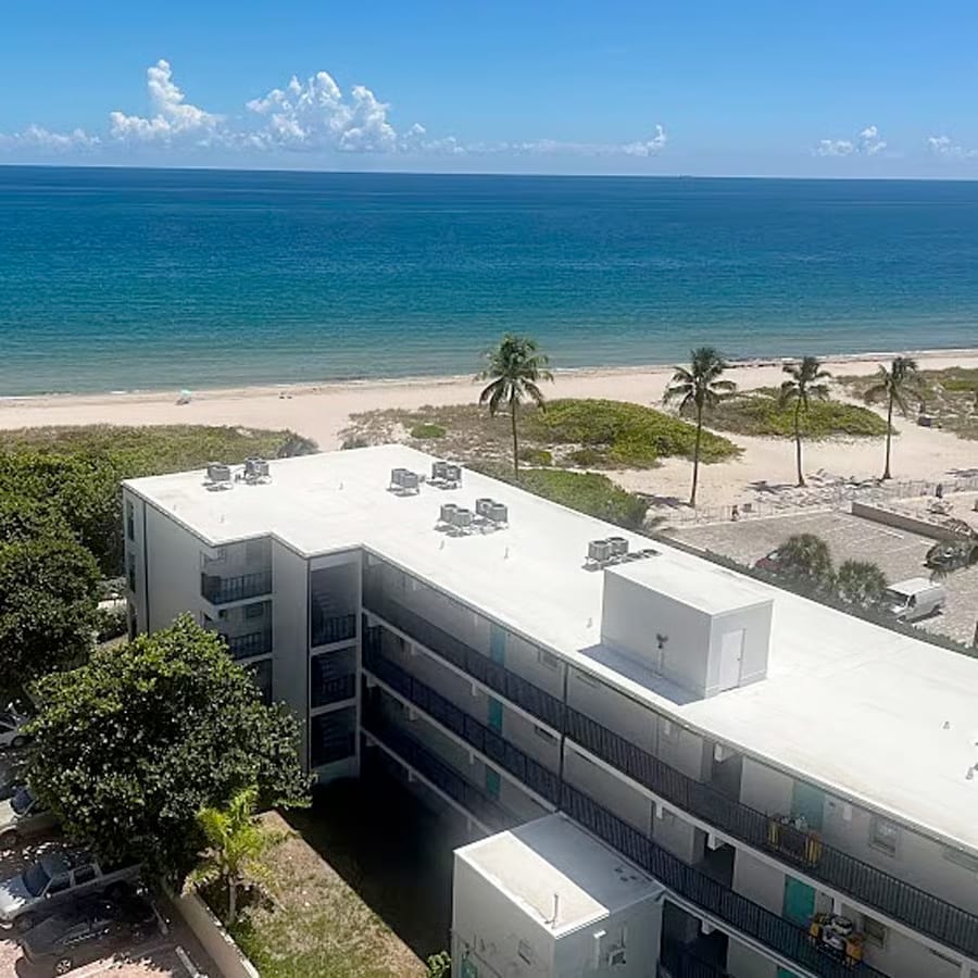 View of a hotel roof with palm trees, beach and ocean in the background.